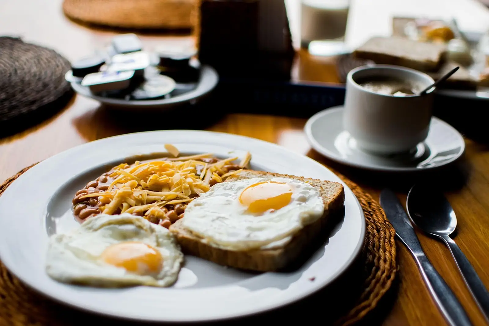 Assiette de petit-déjeuner avec deux œufs au plat, une tartine, des haricots et du fromage râpé, un café à côté