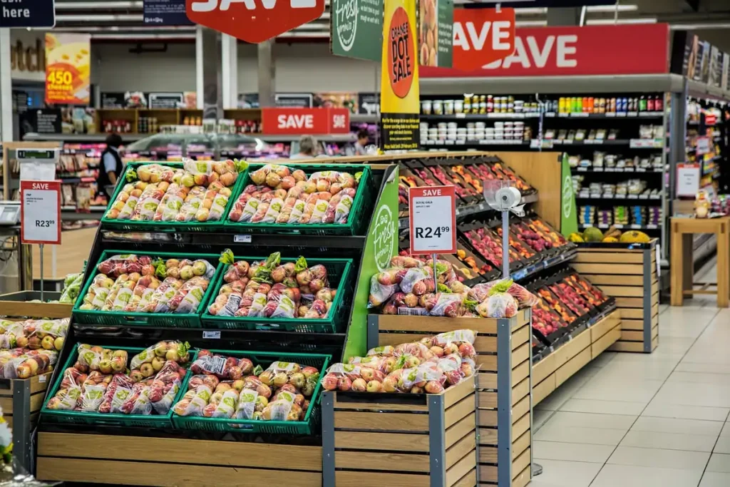Rayon de pommes en sachets dans un supermarché, sous des affiches rouges de promotion et des étiquettes de prix
