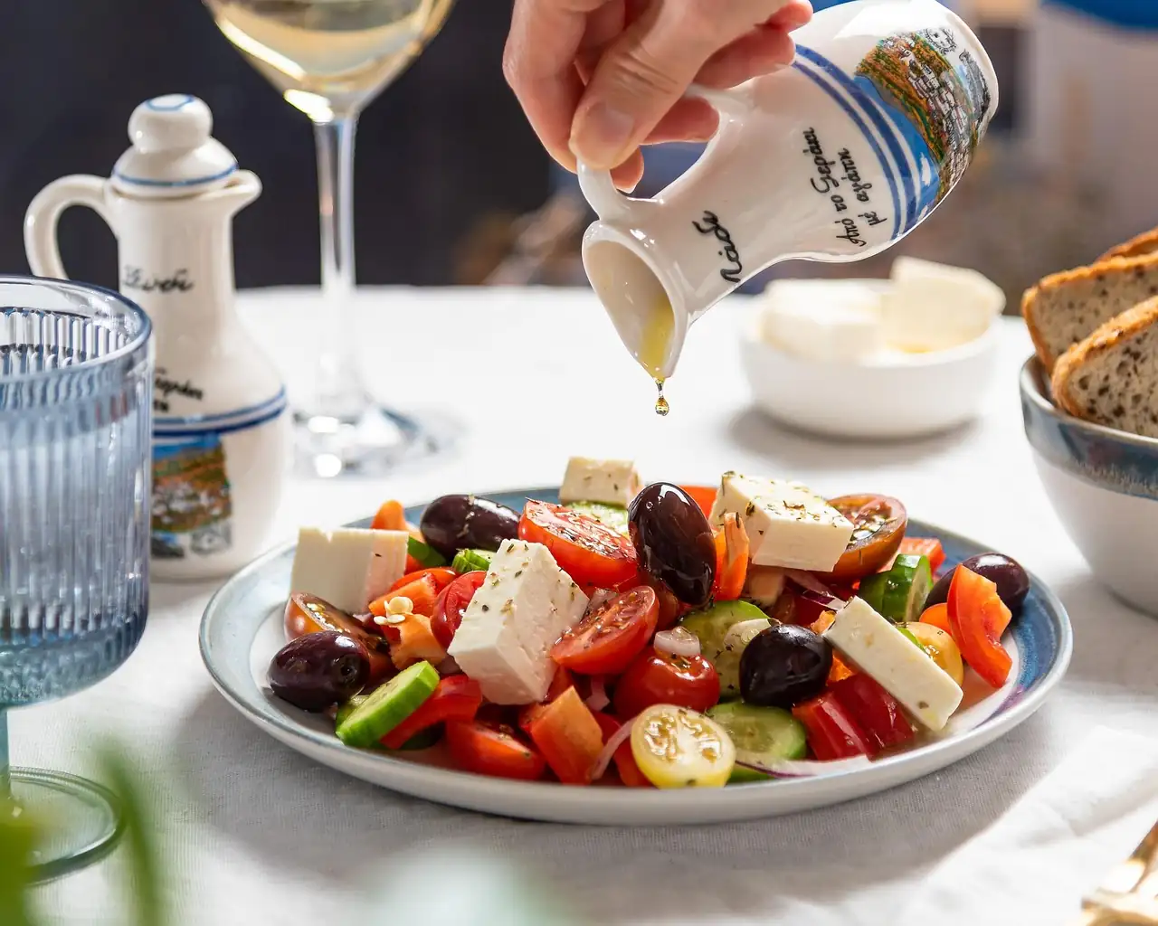 Salade grecque à la feta, tomates et olives, arrosée d'huile d'olive versée d'une petite cruche