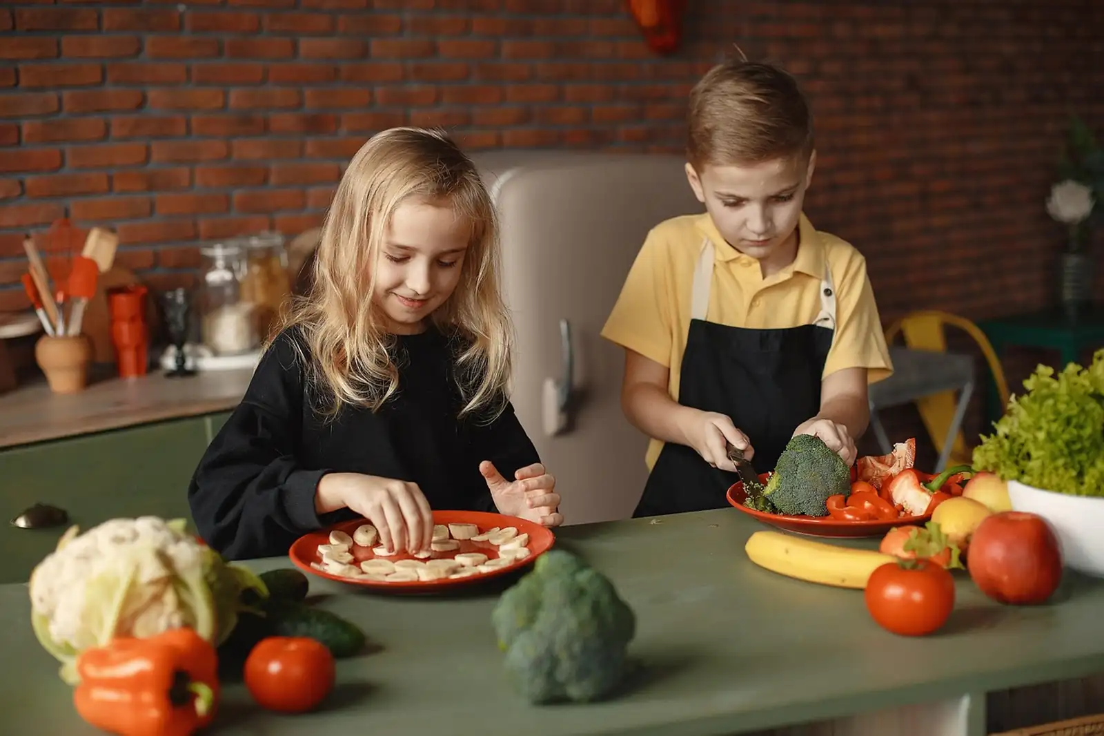 Deux enfants en cuisine, l'un coupe du brocoli, l'autre dispose des rondelles de banane dans une assiette