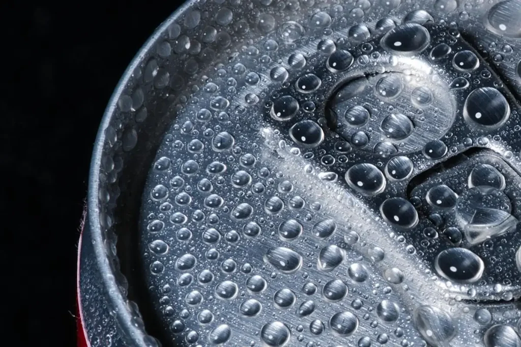 Gros plan sur le dessus d’une canette métallique couverte de gouttes de condensation, sur fond noir