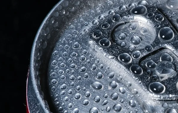 Gros plan sur le dessus d’une canette métallique couverte de gouttes de condensation, sur fond noir