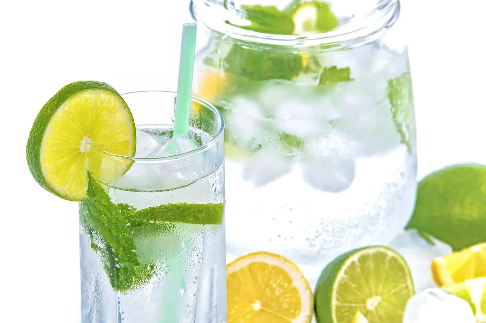 Verre d’eau glacée avec rondelle de citron vert, menthe et paille, devant une carafe et des agrumes coupés