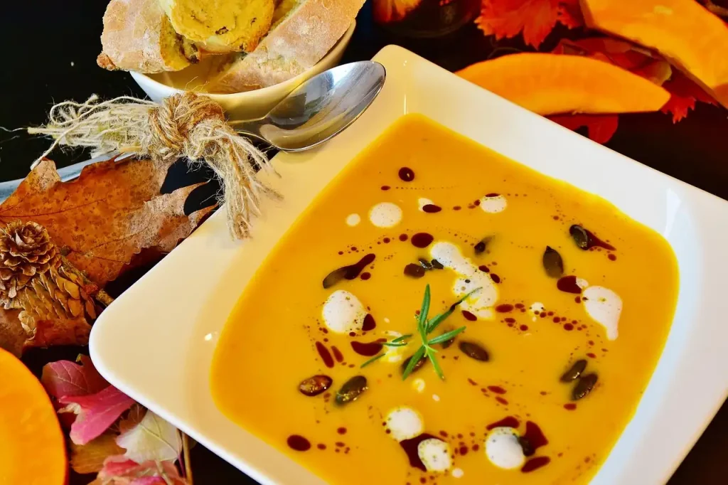 Velouté de potiron dans une assiette carrée, entouré de feuilles d'automne, de pain et de quartiers de courge