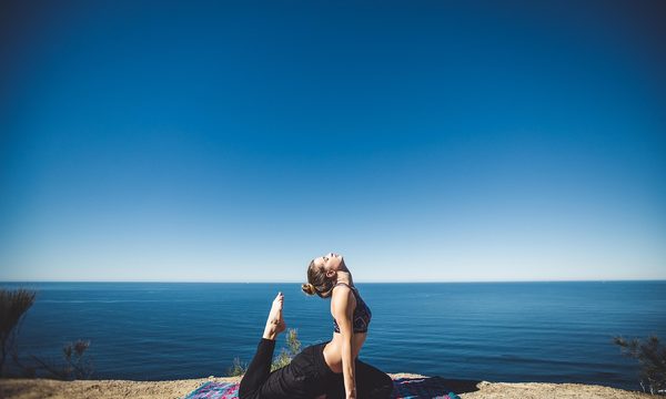 Femme pratiquant le yoga et l'étirement face à l'océan, posture de relaxation en extérieur