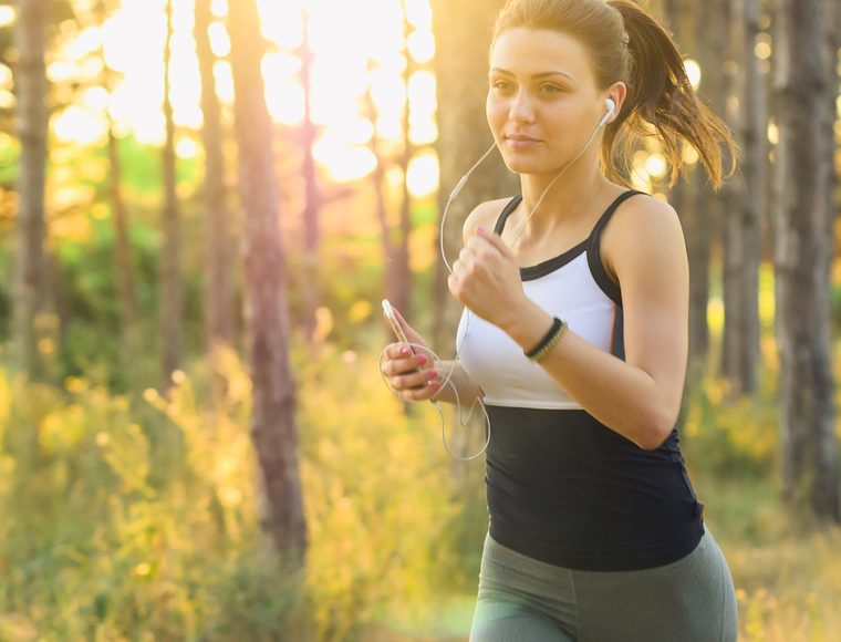 Femme souriante en tenue de sport pratiquant la course à pied en pleine nature, lumière dorée du matin